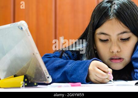 Preteen schoolgirl doing her homework with digital tablet at home. Child using gadgets to study. Education and distance learning for kids Stock Photo