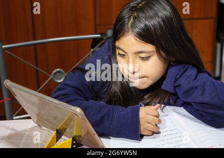 Preteen schoolgirl doing her homework with digital tablet at home. Child using gadgets to study. Education and distance learning for kids Stock Photo