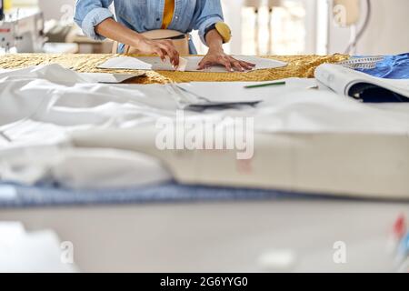 African-American seamstress draws pattern on fabric with tailors chalk at large cutting table Stock Photo
