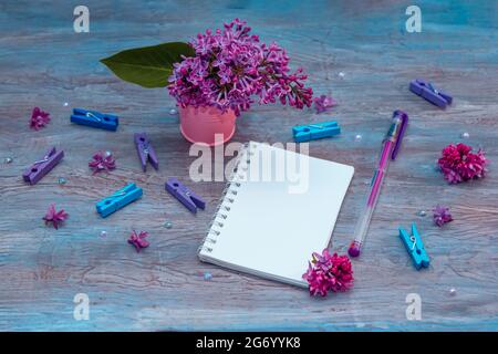 Blank notebook, pencils, lilac flowers and colorful pegs on vintage wooden painted blue background Stock Photo