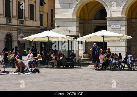 People sitting in a pavement cafe and a street artist painting in St Lawrence Square in the historic centre of Genoa, Liguria, Italy Stock Photo