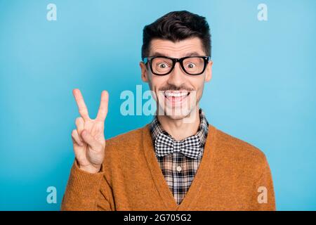 Photo of cheerful handsome young man hold v-sign good mood nerd geek isolated on blue color background Stock Photo