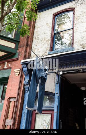 A large pair of denim jeans hanging to dry from a pole outside a storefront, in a city. Stock Photo