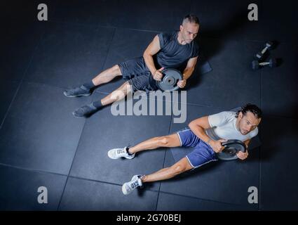 cropped top portrait of two serious men doing weight lifting exercise at indoor gym. up view of people hard fitness training focused and concentrated. Stock Photo