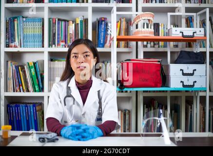 Young Asian doctor in a white coat and gloves sitting in the library Stock Photo