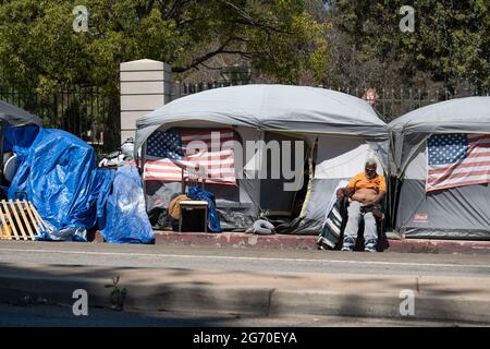 Los Angeles, CA USA - Julyl 3, 2021: A homeless veteran sitting outside his tent on the permieter of the Veterans Administration grounds Stock Photo