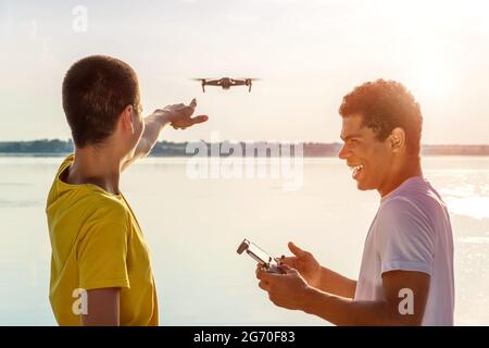 Two young bloggers operating drone with controller standing near the river Stock Photo