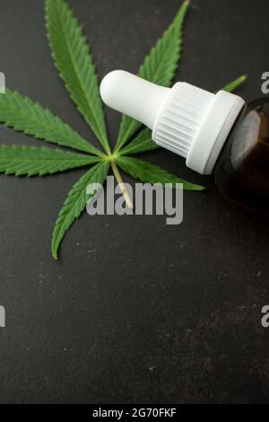 Glass brown bottle of dropper with some cannabis leaves on a black wooden table with copy space Stock Photo