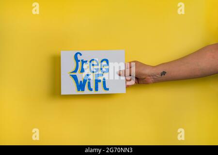 A closeup shot of a woman holding a paper with the word 'FREE WIFI' on a yellow background Stock Photo