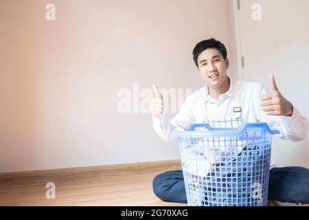 Asian man husband working homework.He is preparing clothes in basket to wash to washing machine for service lifestyle family togetherness in home Stock Photo