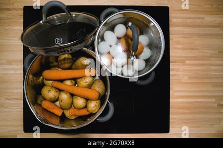 boiling hen eggs and vegetables in pans on ceramic inductive induction cooker stove hob Stock Photo
