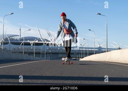 Street fashion and urban lifestyle: hipster man in trendy casual clothes on longboard on city road Stock Photo