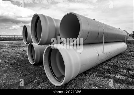 Stacked water main pipe with bell fitting next to an exposed trench for installation Stock Photo