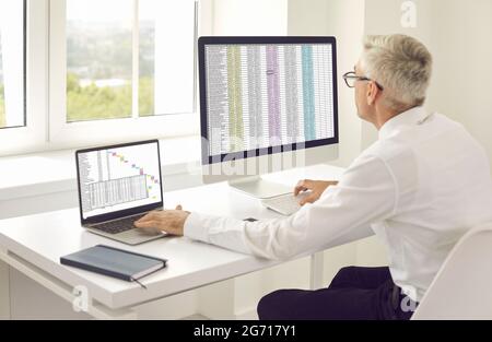 Man sitting at office desk and making Gantt chart using laptop and desktop computer Stock Photo