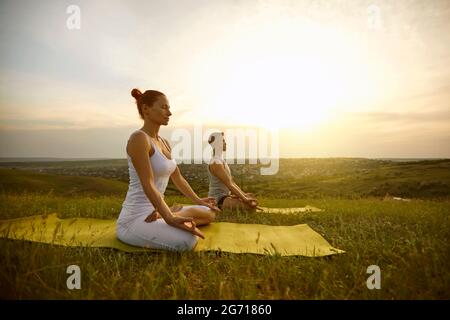 Couple sitting in lotus position with eyes closed, meditating and practicing yoga on nature together Stock Photo