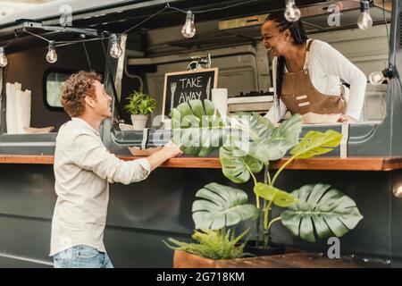 African chef woman taking order from customer at food truck outdoor - Focus on man face Stock Photo