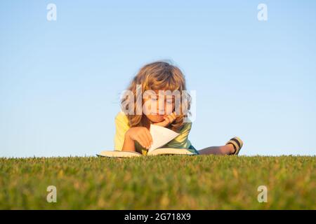 Smart child reading book, laying on grass in field on sky and grass field. Portrait of clever kids. Stock Photo