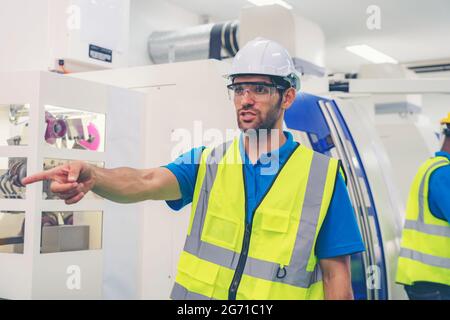 Male industrial engineer or technician worker wear face mask with safety and hard helmet training trainee assistant using control machine operating co Stock Photo