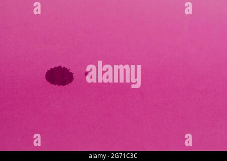 Minimalist composition with dark spots on a pink background. Two spilled drops of red wine on colored paper. A large and a small stain. Selective focu Stock Photo
