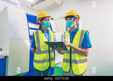 Male industrial engineer or technician worker wear face mask with safety and hard helmet training trainee assistant using control machine operating co Stock Photo