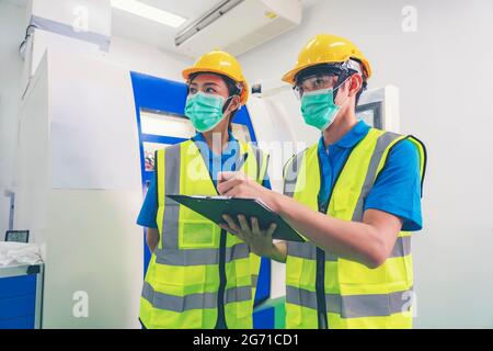 Male industrial engineer or technician worker wear face mask with safety and hard helmet training trainee assistant using control machine operating co Stock Photo