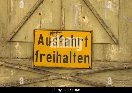 Shabby, scuffed Ausfahrt freihalten (Keep Exit Clear) sign on a weathered wooden door with peeling paint. Stock Photo