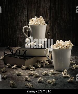 Vertical shot of two cups of popcorn put on books on a table against a wooden background Stock Photo