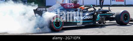Mercedes Benz F1 W10 EQ Power+ racing car with smoking rear tyres burns rubber racing away. Petronas and Ineos sponsor the team: letterbox crop. Stock Photo