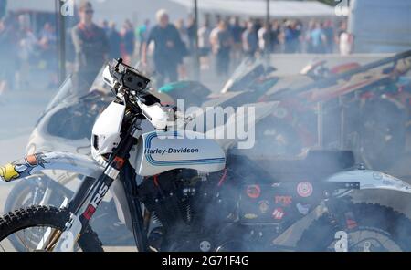 A Harley Davidson off-road sports motorcycle with a white petrol tank sits shrouded in exhaust smoke at the Goodwood Festival of Speed 2021. Stock Photo