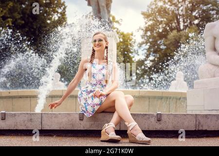 Beautiful Woman sitting on the edge of a fountain on a hot summer day Stock Photo