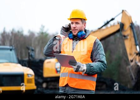 Portrait of a quarry worker standing in front of excavator smiling Stock Photo