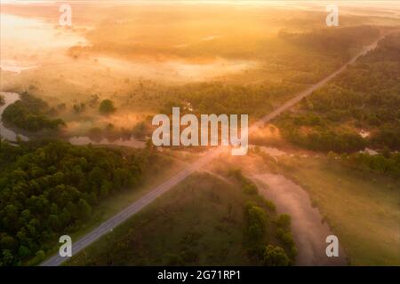 Drone view of the bright dawn over the highway overpass, forest and misty meadow. Stock Photo