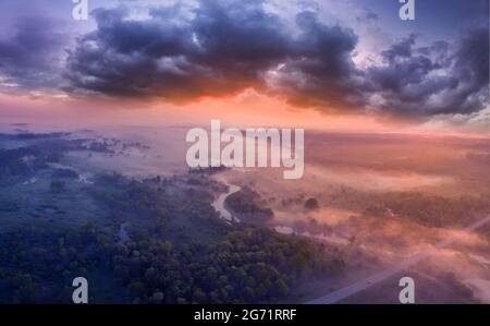 Drone view of the bright dawn over the highway overpass, forest and misty meadow. Stock Photo