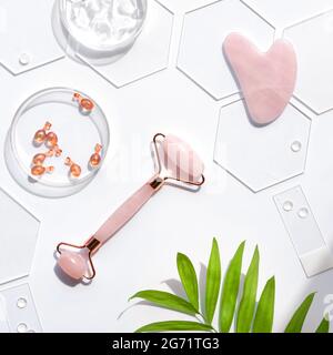 Pink Quarts stone face roller and serum capsules in round glass dish and hexagones. Gua sha stone for beauty facial massage therapy. Natural cosmetics Stock Photo