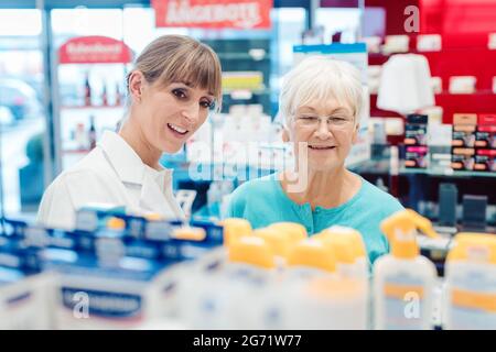 Chemist and customer standing in pharmacy between the shelves talking Stock Photo