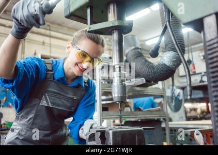 Woman worker in metal workshop using pedestal drill to work on piece Stock Photo