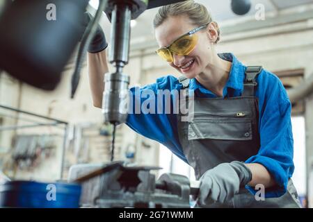 Woman worker in metal workshop using pedestal drill to work on piece Stock Photo