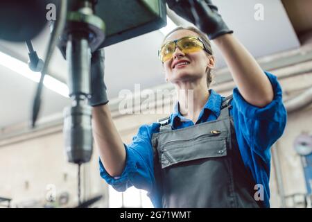 Woman worker in metal workshop using pedestal drill to work on piece Stock Photo