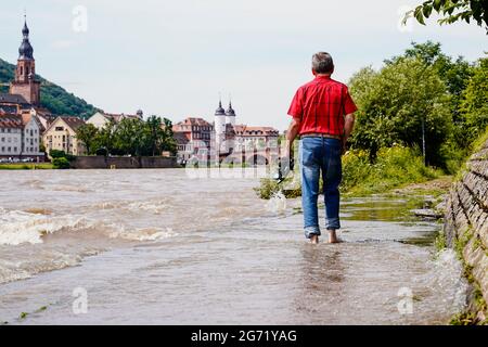 Heidelberg, Germany. 10th July, 2021. A man walks along a section of the Leinpfad flooded by the Neckar. Buildings of the old town can be seen in the background. The water level is expected to rise above the navigation limit on Saturday. Credit: Uwe Anspach/dpa/Alamy Live News Stock Photo