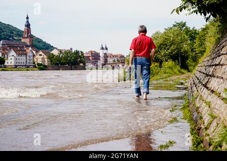 Heidelberg, Germany. 10th July, 2021. A man walks along a section of the Leinpfad flooded by the Neckar. Buildings of the old town can be seen in the background. The water level is expected to rise above the navigation limit on Saturday. Credit: Uwe Anspach/dpa/Alamy Live News Stock Photo