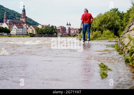 Heidelberg, Germany. 10th July, 2021. A man walks along a section of the Leinpfad flooded by the Neckar. Buildings of the old town can be seen in the background. The water level is expected to rise above the navigation limit on Saturday. Credit: Uwe Anspach/dpa/Alamy Live News Stock Photo