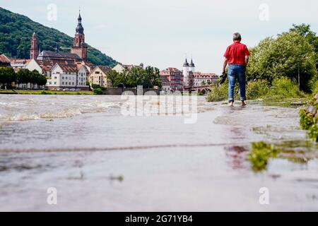 Heidelberg, Germany. 10th July, 2021. A man walks along a section of the Leinpfad flooded by the Neckar. Buildings of the old town can be seen in the background. The water level is expected to rise above the navigation limit on Saturday. Credit: Uwe Anspach/dpa/Alamy Live News Stock Photo