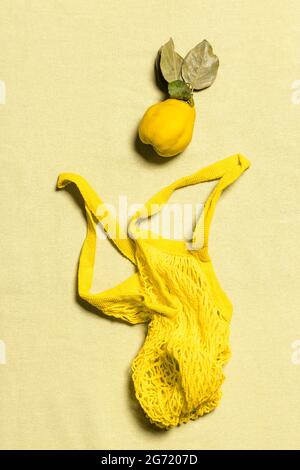 Quince apple with leaves and yellow mesh bag on wrinkled natural pastel colored linen background. Organic fruit has natural defects. Conscious consume Stock Photo