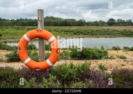 Orange life buoy ring beside a deep water quarry lake, UK Stock Photo