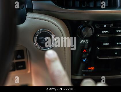 Finger pressing button the start button, stop the engine in the luxury car. The man's finger is pressing down. Owner and dealership concept. Stock Photo