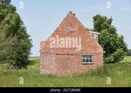 Old decaying shed with red bricks against a blue sky near Ferwert in The Netherlands. Stock Photo