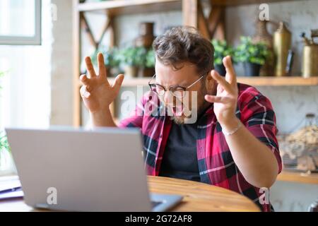 Young man yells at the laptop monitor. He has a big problem. Overworking concept. Stock Photo