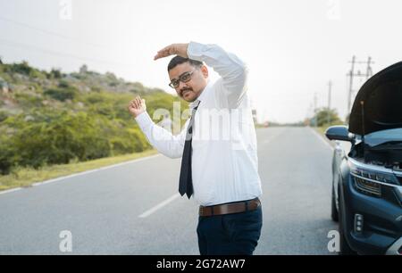 Businessman asking for lift or hitchhiking due to car breakdown while traveling - concept of asking help while commuting Stock Photo