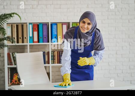 Smiling Arabian woman cleaning a table in the office Stock Photo