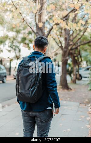 Back view of a young stylish male student wearing a black backpack and holding a notebook Stock Photo